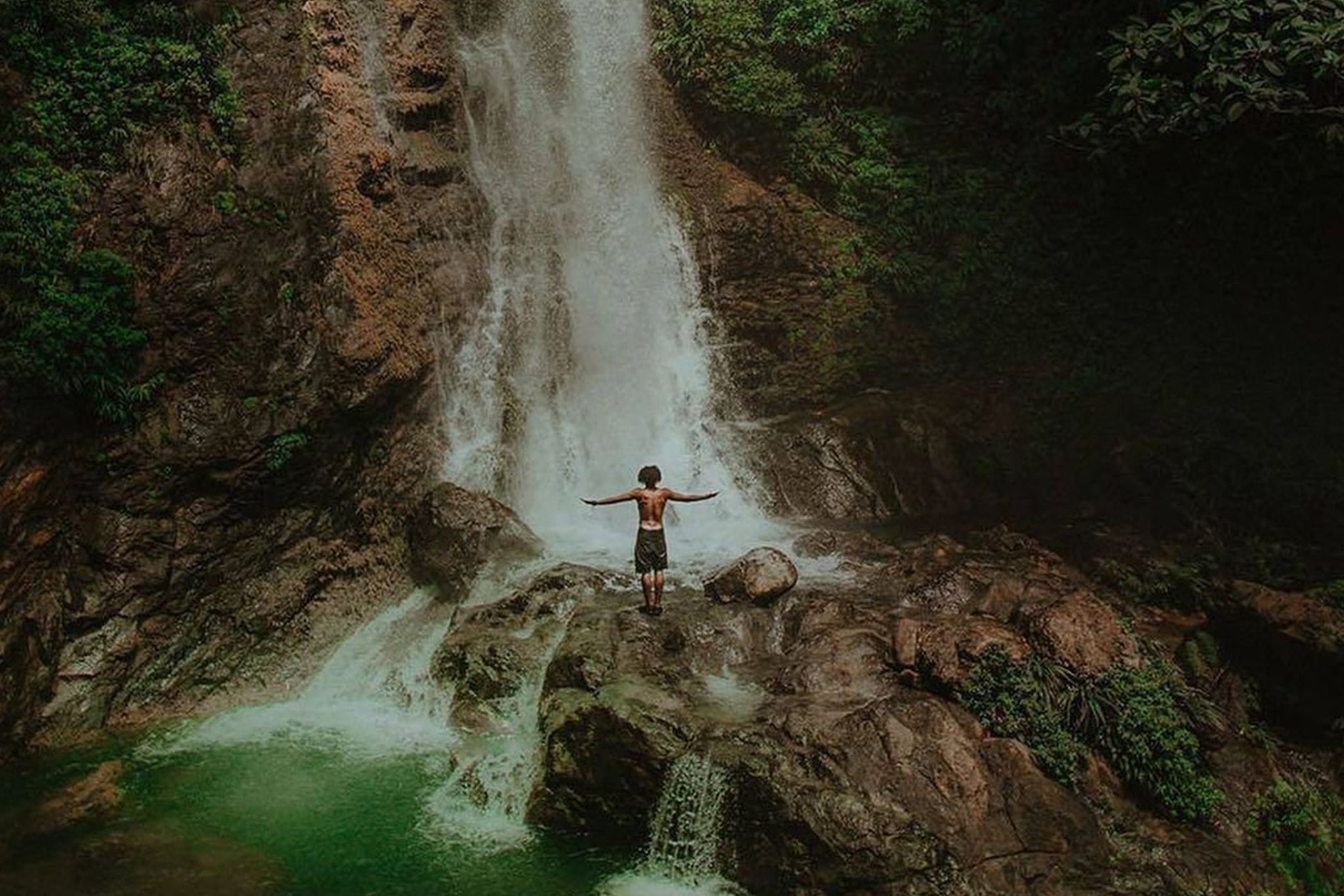 A man stands in front of a stunning waterfall in the Panama rainforest.