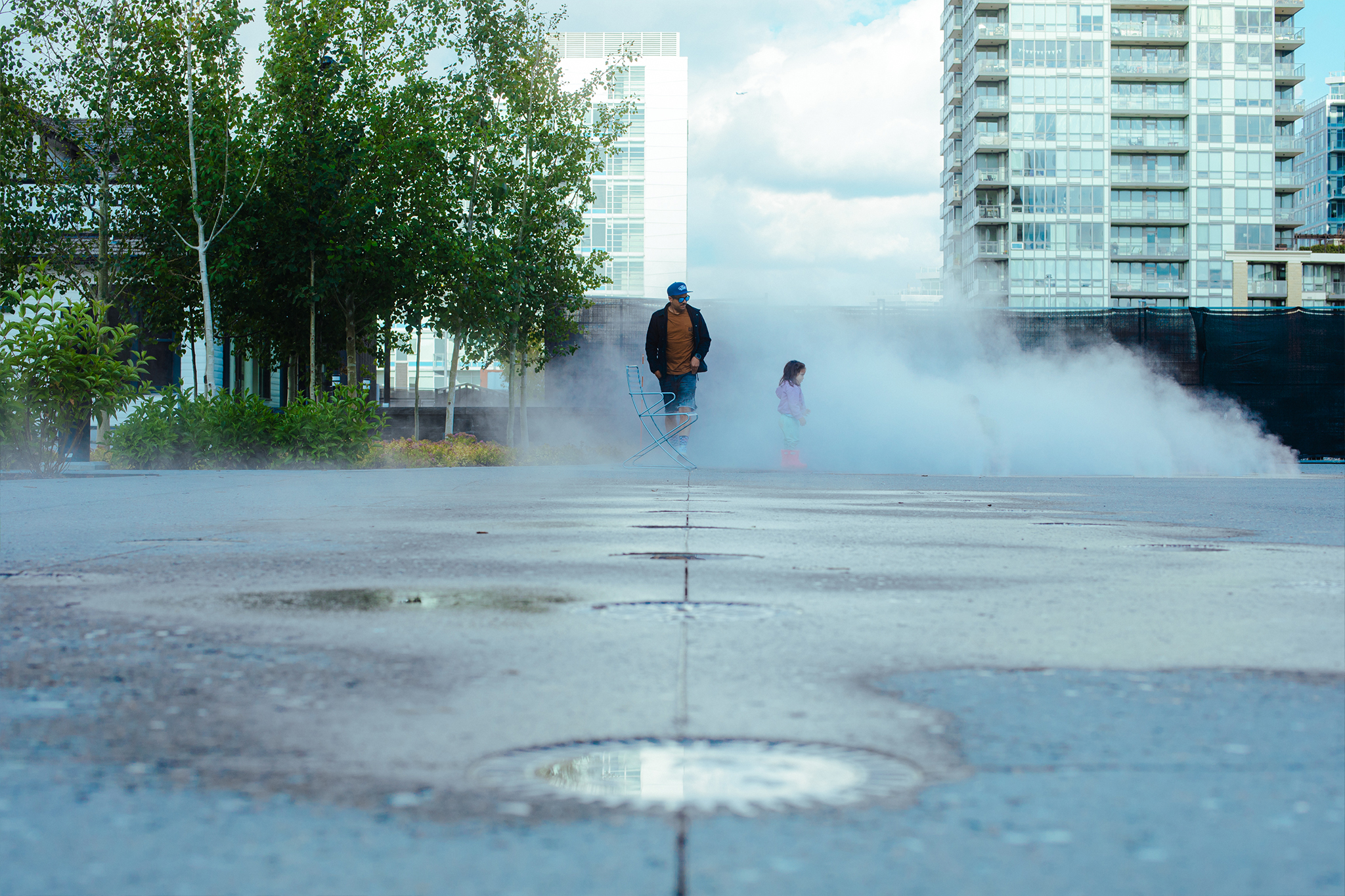 A man and child in red boots enjoy the water mist feature newly installed at Eau Claire Plaza.